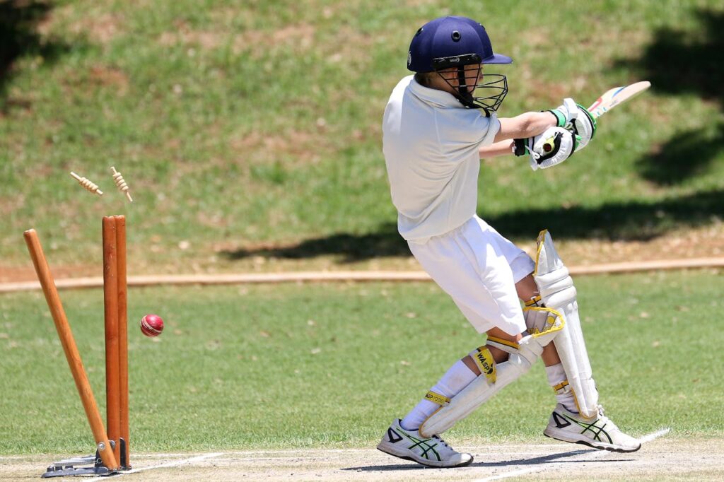 Young cricket player in full gear performing a sweep shot on a sunny day outdoors.